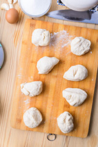 Boules de pâte crue disposées sur une planche en bois, prêtes à être façonnées.