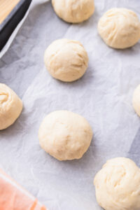 Boules de pâte à pain crue disposées sur une plaque recouverte de papier cuisson.