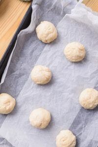 Boules de pâte crue disposées sur une plaque de cuisson recouverte de papier sulfurisé.