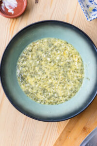 Bol de sauce verte crémeuse à l’ail et aux herbes sur une table en bois.