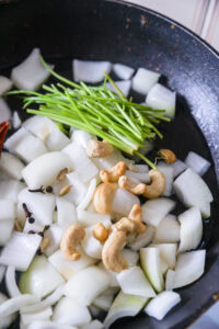 Malai Kofta - Ajouter un peu d’eau, puis incorporer la cannelle, les clous de girofle, les gousses de cardamome, les noix de cajou, le piment rouge sec et les tiges de coriandre.