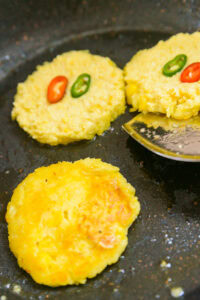 Oksusu Jeon - Chauffer une poêle, ajouter l’huile de cuisson, faire dorer les galettes de maïs, déposer les rondelles de piments vert et rouge dessus en garniture, puis les faire cuire jusqu’à ce qu’elles soient bien saisies.