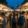 Foule dans un marché de street food asiatique animé au crépuscule, stands fumants des deux côtés.