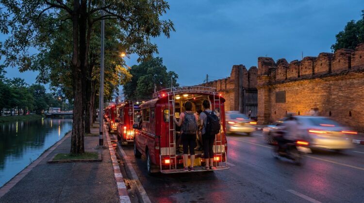 Taxis rouges bondés près d’un vieux mur en briques, au bord d’un canal, au crépuscule.
