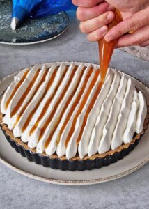 Banoffee pie vegan à la ganache café (sans gluten) - Dépose quelques rondelles de banane caramélisée sur le dessus, puis fais couler le reste de la sauce au caramel entre les bandes de crème fouettée pochée.