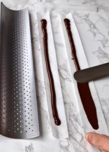 Bûche sans gluten chocolat et châtaigne - Fais fondre le chocolat noir et étale-le finement sur des bandes d’acétate pour gâteau ou des bandes de papier cuisson, de 2,5 cm de large et 30 cm de long.