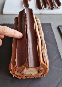 Bûche sans gluten chocolat et châtaigne - Pose les bandes d’écorce en chocolat sur les lignes de crème pâtissière pour recouvrir entièrement la bûche. Saupoudre une fine couche de sucre glace avant de servir ou de couper.