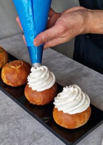 Buns à la crème sans gluten à la pistache - Poche la crème fouettée sur les brioches avec une douille cannelée en mouvement circulaire en spirale.