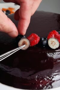 Entremets sans gluten vegan - Transfère l’entremets sur un support à gâteau. Décore avec des baies tranchées et de la menthe disposées en motif. Regarde la vidéo pour les détails.