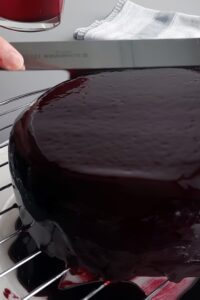 Entremets sans gluten vegan - Fais chauffer le glaçage aux fruits au cassis à environ 50°C. Démoule l’entremets congelé et place-le sur la grille. Étale le glaçage aux fruits chaud et utilise une spatule pour lisser la surface. Assure-toi de placer un plateau ou une assiette sous la grille pour récupérer ce qui s’égoutte.
