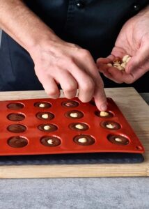 Ferrero Rocher sans gluten : comment en faire - Prépare un moule en silicone en forme de dôme de 2-3 cm de diamètre. Remplis chaque empreinte à moitié avec la ganache tiède, puis place une noisette entière ou une demi-noisette au milieu. Mets au congélateur au moins 15 minutes.