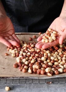 Ferrero Rocher sans gluten : comment en faire - Retire la peau en frottant les noisettes entre tes deux mains. Mets de côté 25 noisettes entières et hache le reste.