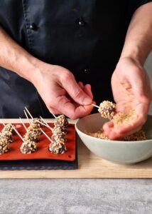 Ferrero Rocher sans gluten : comment en faire - Démoule la ganache congelée et superpose deux demi-sphères pour former une boule de 2-3 cm. Roule et presse dans les noisettes torréfiées hachées. Pique un cure-dent dans chaque boule, puis mets au frais ou au congélateur.