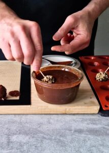 Ferrero Rocher sans gluten : comment en faire - Tiens la pointe du cure-dent puis trempe les boules de chocolat froides dans l’enrobage noisette-chocolat. Laisse le chocolat s’égoutter quelques secondes, puis mets au réfrigérateur.