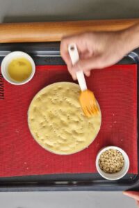 Flan sans gluten aux agrumes - Badigeonne de dorure à l’œuf, répartis les pignons de pin uniformément sur le dessus, puis pique quelques trous dans la croûte avec une fourchette.