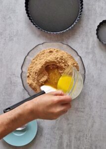 Fond de tarte vegan sans gluten aux biscuits type Graham - Mélange les miettes et le beurre fondu sans lactose dans un bol jusqu’à obtenir un mélange homogène.
