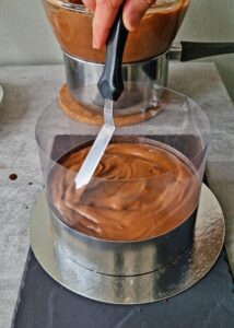 Gâteau au chocolat vegan sans gluten à la mangue - Ajoute une couche de mousse mangue-chocolat sur le biscuit. Utilise une spatule coudée pour l’étaler uniformément sur environ 1,3 cm d’épaisseur. Tapote doucement pour lisser les éventuelles poches d’air.