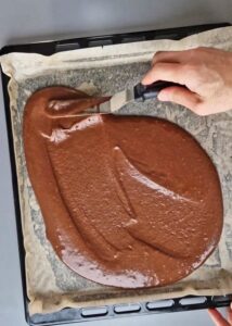 Gâteau au chocolat vegan sans gluten à la mangue - Verse la pâte uniformément sur la plaque de cuisson et étale-la en une couche fine et régulière d’environ un demi-centimètre d’épaisseur.