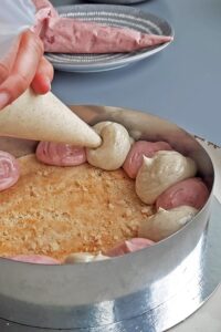 Gâteau aux fraises sans gluten - Place le premier biscuit au fond, imbibe-le de sirop de sucre, puis poche alternativement la crème mousseline à la vanille et à la fraise sur les côtés.