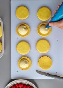 Gâteau macaron mangue framboise (sans gluten) - Poche une noisette de ganache montée à la mangue au centre d’une coque.
