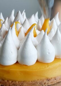 Gâteau mangue passion (sans gluten) - Retire le cercle à gâteau et transfère le gâteau sur un support à gâteau ou une assiette. Poche la meringue avec une douille ronde sur le dessus du gâteau. Poche le reste de la crème mangue-fruit de la passion sur le dessus de la meringue.