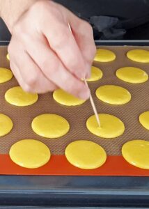 Macarons sans lactose à la crème au citron (sans gluten) - Tape la plaque quelques fois pour aplatir la pâte, puis perce les bulles en surface avec un cure-dent.