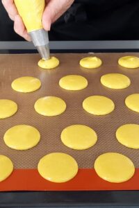 Macarons sans lactose à la crème au citron (sans gluten) - Avec une douille n°10, poche la pâte en disques d’environ 4 cm de diamètre sur une plaque recouverte d’un tapis Silpat ou d’un tapis en silicone.