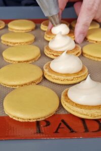 Macarons sans lactose à la crème au citron (sans gluten) - Remplis une poche à douille avec la crème au citron froide, puis poche une noisette de garniture au centre d’une coque.