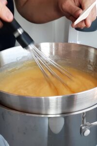 Mini tarte au citron meringuée sans gluten - Mélange le jus de citron, le zeste, la fécule de maïs, les œufs et le sucre dans un saladier. Fais cuire au bain-marie en fouettant constamment jusqu’à épaississement. Retire du feu.