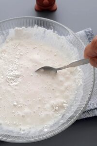 Pain sans gluten en cocotte, deux méthodes - Mélange la farine sans gluten, l’eau et la levure, puis transfère dans un bocal légèrement couvert pour laisser entrer l’air.