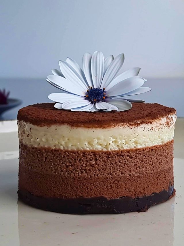 Gâteau mousse au chocolat vegan à trois couches, poudré de cacao et décoré d’une fleur blanche