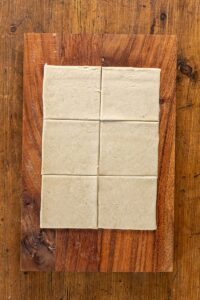 Pâte brisée étalée et découpée en carrés sur une planche