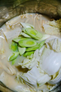 Tōnyū nabe - Dès les premiers frémissements, ajouter le chou chinois, la mizuna, le poireau et le sésame moulu.