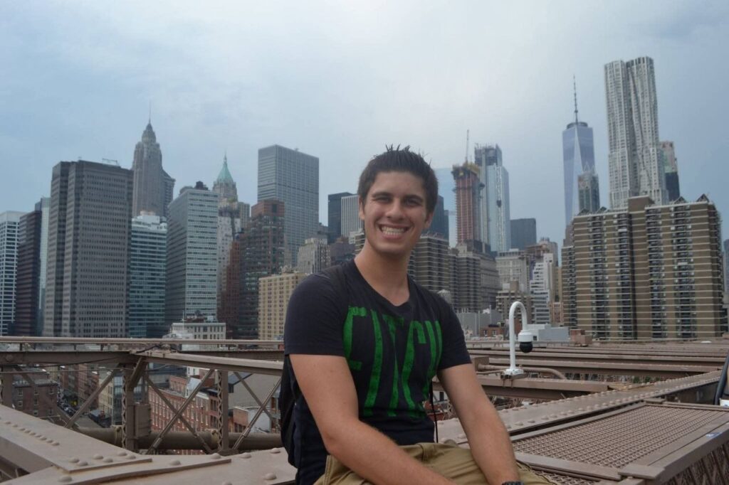 Marc Winer siddende på Brooklyn-broen i 2017 med Lower Manhattans skyline bag sig