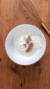 Farine, bicarbonate, sel et cannelle réunis dans un bol, avec un fouet