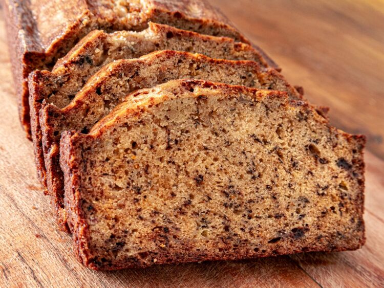 Tranches de banana bread moelleux devant le cake entier, sur une planche en bois