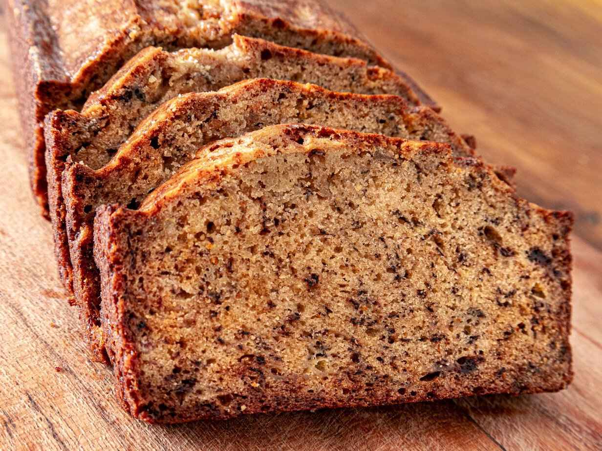 Tranches de banana bread moelleux devant le cake entier, sur une planche en bois
