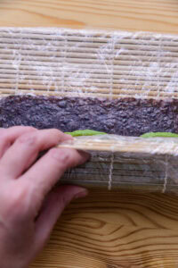 California roll - Soulever le bord de la natte du côté de la garniture et le rabattre par-dessus, pour enfermer la garniture dans la nori, en pressant légèrement.