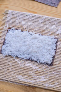 California roll - Presser une portion de riz en couche régulière sur toute la demi-feuille, jusqu'aux bords, en travaillant d'un long côté vers l'autre.