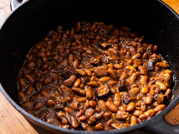 Haricots à la bostonienne dans une cocotte en fonte noire, sauce brune brillante et cubes de lard salé
