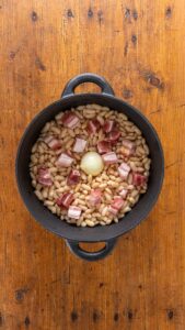 Cocotte en fonte garnie de haricots blancs, de cubes de lard salé et d'un oignon entier