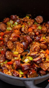 Jambalaya - Poursuivre la cuisson en remuant et en raclant le fond à la spatule en bois : l'humidité des légumes décolle les sucs bruns laissés par la viande. Cuire jusqu'à ce que tous les légumes soient tendres et bien caramélisés, d'un brun soutenu, en veillant à ne pas les brûler.