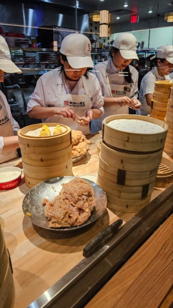 Cuisiniers pliant des xiao long bao à la main derrière une vitre chez Nan Xiang, New York