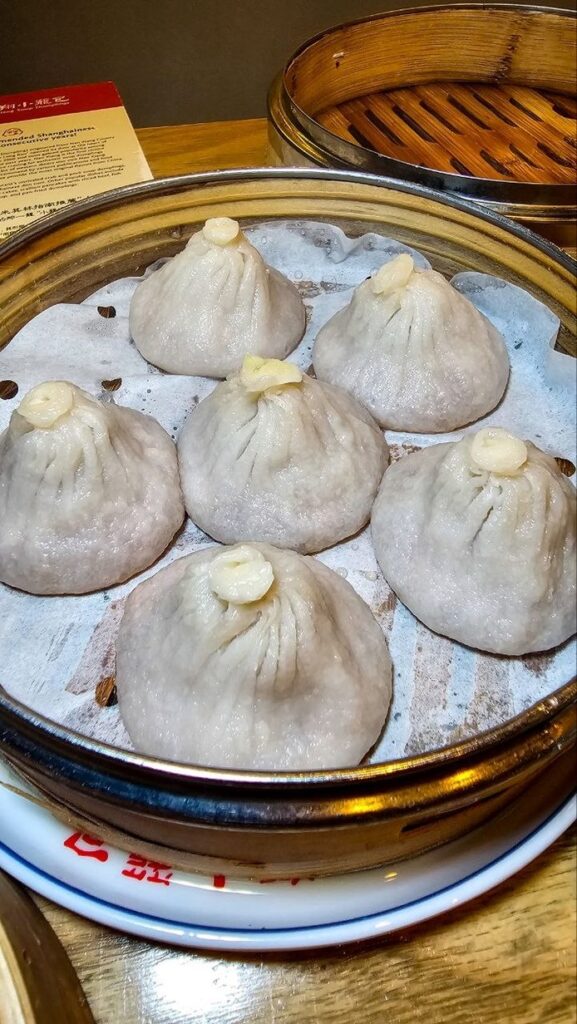 Six xiao long bao coiffés d'une lamelle de truffe dans un panier vapeur chez Nan Xiang, New York